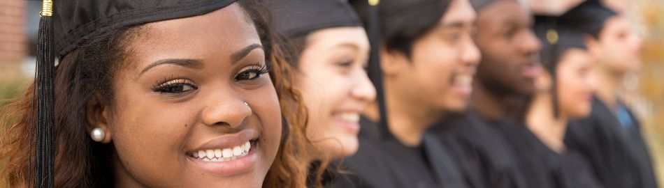 Students wearing graduation caps, smiling, and sitting in a row of seats 
